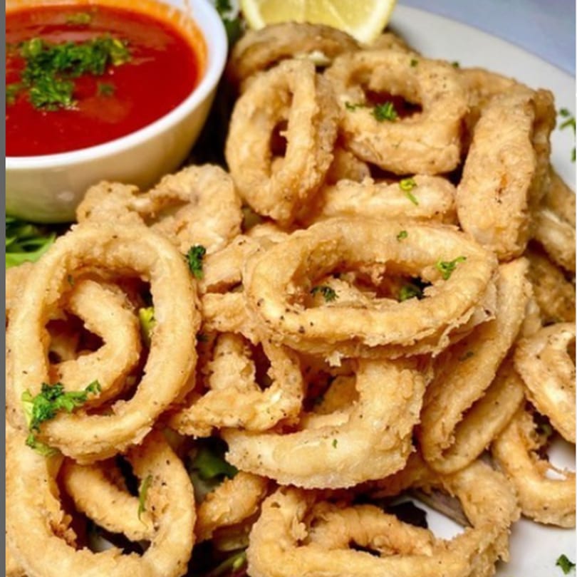 Crispy fried calamari rings with a side of red marinara sauce and a lemon wedge.