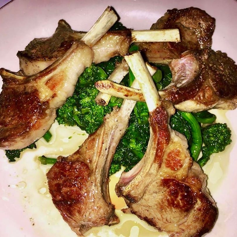Grilled lamb chops with bones, served over green broccoli and a creamy white sauce on a light plate.