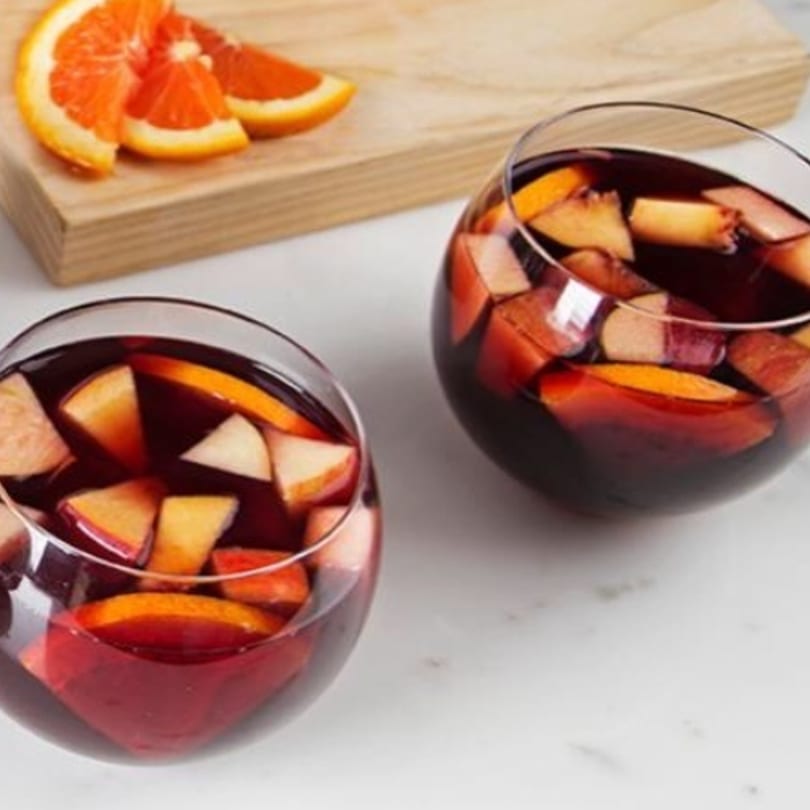 Two glasses of red sangria with fruit, and orange slices on a wooden board.