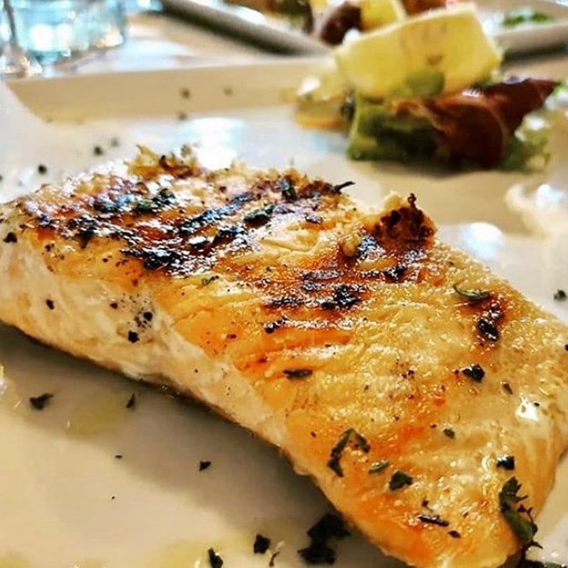Grilled salmon fillet seasoned with herbs and spices, served on a white plate with a side salad.