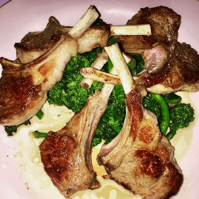 Grilled lamb chops with broccoli rabe and a creamy sauce on a white plate.